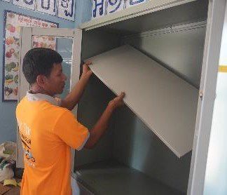 A staff member in an orange shirt fits a shelf into a new steel cabinet