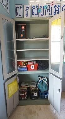 An open cabinet in a classroom holds a speaker, teaching materials and storage baskets on its shelves