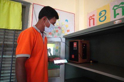 A staff member in an orange shirt places a speaker on a cabinet shelf in a classroom
