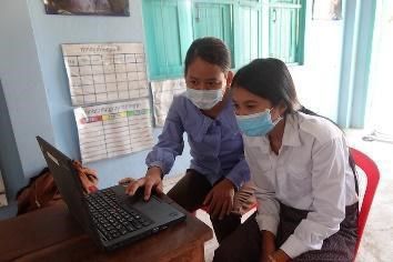 Two teachers practise using a laptop together at a school desk
