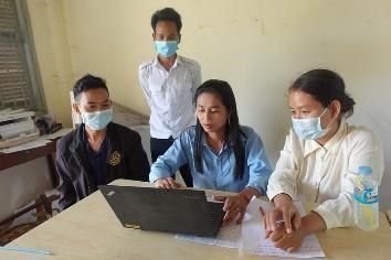 Teachers and a trainer sit around a laptop at a table during a follow-up visit