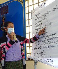 A teacher holds a microphone and points to notes written on a flip chart during the meeting