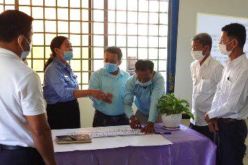 Officers and principals stand around a table signing papers at the project kick-off meeting