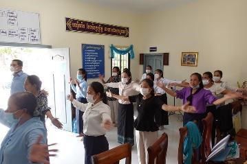 Workshop participants stand in a group and stretch their arms out during a dancing and music activity