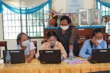 Preschool teachers work on laptops at a workshop table while a trainer leans in to help