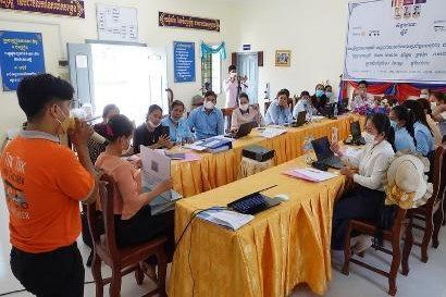 A trainer in an orange shirt speaks to preschool teachers seated at long tables during the first workshop