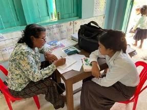 Two women sit on red chairs and fill in an assessment sheet together in a classroom