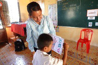 A teacher helps a young student hold up a picture card during a classroom activity