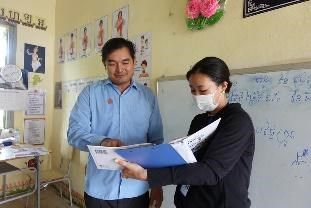 A school official and a project staff member look through a folder of resources in a classroom