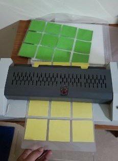 Small green and yellow cards come out of a laminating machine on a table