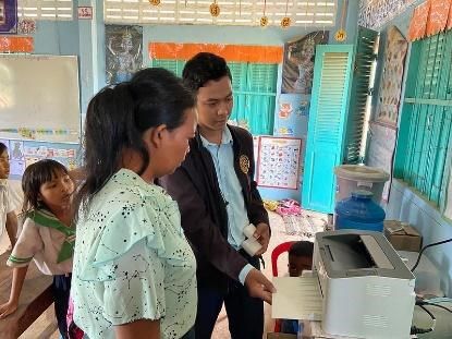 A teacher and a visitor look at a new printer and a printed page while a student watches