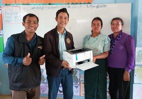 Four people smile as they hold a new printer in the Tram Pair preschool classroom