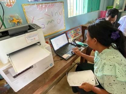 A teacher uses a laptop connected to the new printer and holds a printed worksheet