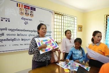 A teacher shows a large colourful board game to seated participants during the second workshop