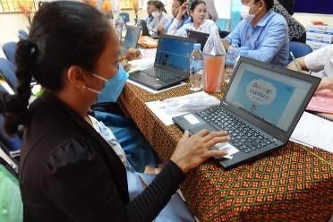 A teacher in a black jacket uses a laptop showing the Digital Library at a long workshop table