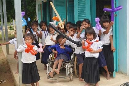 Young students in school uniform hold balloon animals and smile outside their classroom