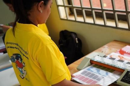 A woman in a yellow shirt feeds sheets of colour cards into a laminating machine