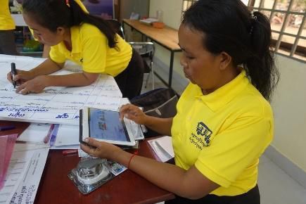 A teacher in a yellow shirt uses a tablet at a table covered with flip chart paper