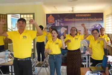 Workshop participants in yellow shirts raise their arms and move together during a dancing and music activity