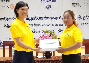 Two women in yellow shirts exchange a boxed tablet in front of the workshop banner