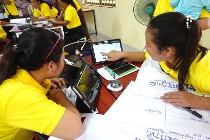 Teachers in yellow shirts practise searching on tablets at a table covered with flip chart paper