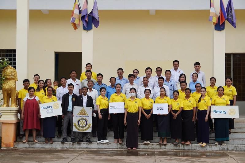 Meeting participants in yellow shirts and school staff pose for a group photo holding Rotary signs