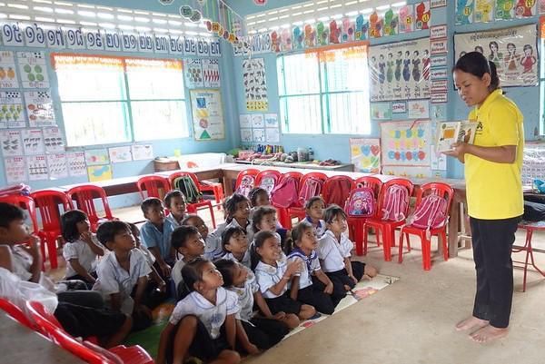 A staff member in a yellow shirt shows a picture book to preschool children sitting on the floor