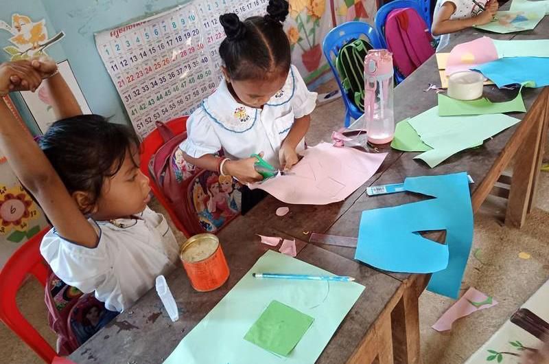 A young student cuts coloured paper at a craft table in a preschool classroom