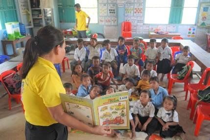 A teacher in a yellow shirt reads a picture book to preschool children sitting on the floor