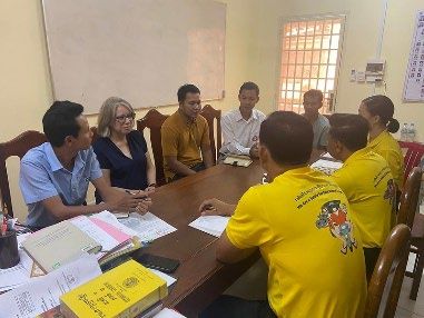 Staff in yellow shirts and officials sit around a wooden table in a meeting about the project