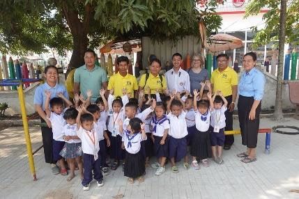 Staff, teachers and young students in uniform pose together outdoors, with the children raising their arms
