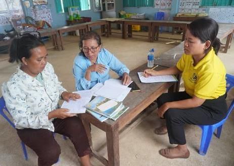 Three women sit around a table reviewing assessment papers together in a classroom