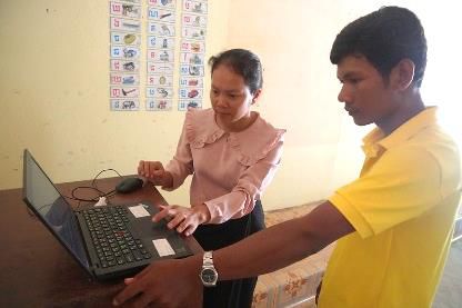 A teacher in a pink blouse and a staff member in yellow work together at a laptop