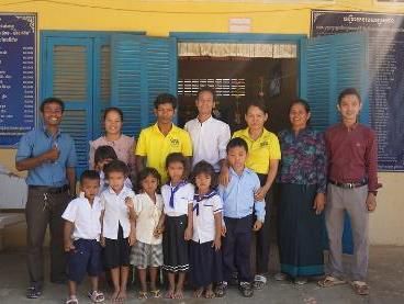 Teachers, staff and young students in school uniform pose together in front of a school building