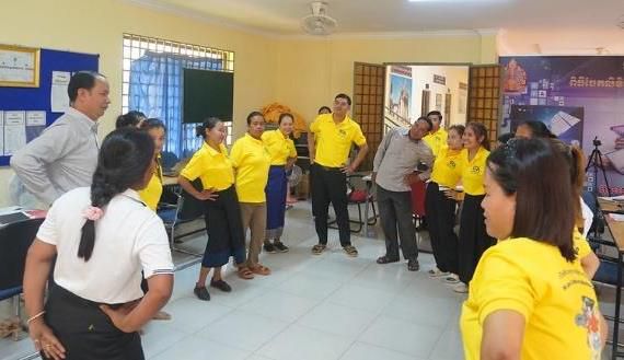 Workshop participants stand in a circle in a classroom while taking part in a group game