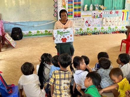 A teacher holds up a picture card to young children sitting on the floor of a classroom
