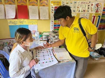 A staff member in yellow leans over a table to look at a board game with a teacher