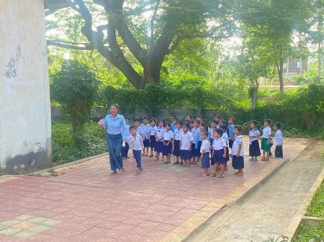 A teacher in blue leads a line of young pupils in school uniform in an outdoor activity