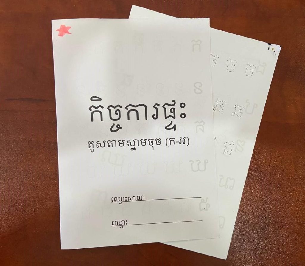 Printed activity booklet with a Khmer title on its cover, resting on a wooden table
