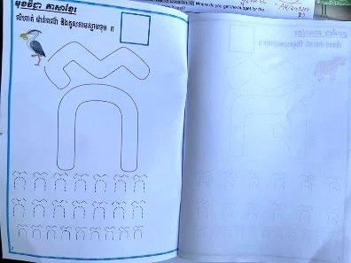 An open printed booklet with a large Khmer letter to trace and rows of practice letters