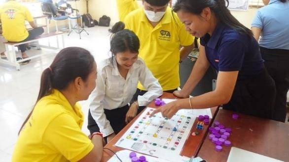 Teachers play a colourful board game with purple counters on a table at the workshop