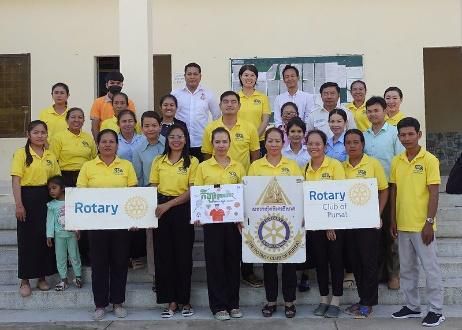 Teachers, officials and staff in yellow shirts pose on school steps, some holding Rotary Club signs