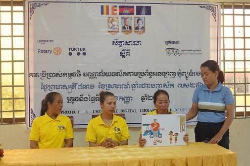 Staff in yellow shirts sit at a draped table under the workshop banner while one holds up a picture card