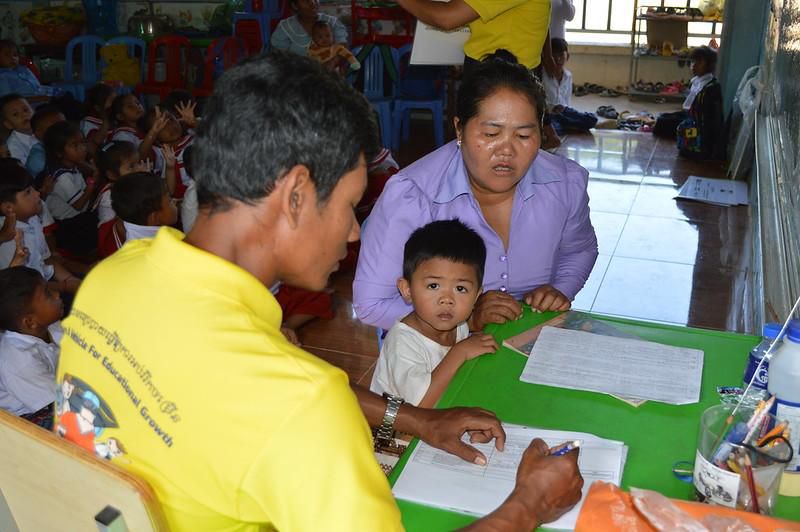 A teacher is interviewed at a school desk during the baseline survey while preschool children sit nearby