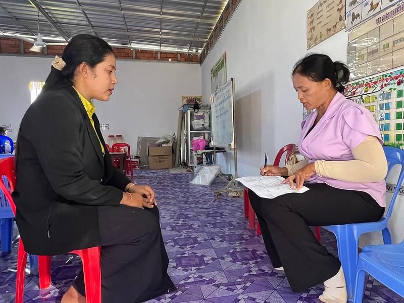 A project staff member in a dark jacket sits with a teacher completing the classroom assessment sheet