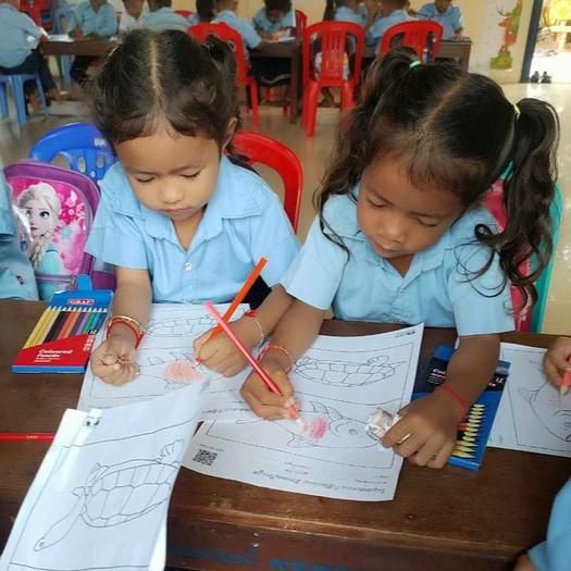 Two preschool girls color a worksheet with the colored pencils supplied by the project