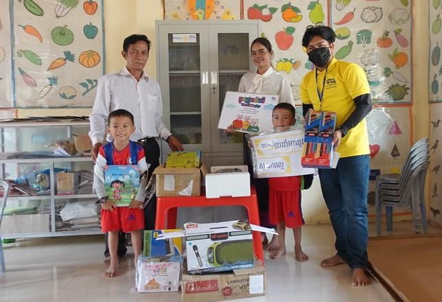 Project staff and a school director hand over boxes of equipment and storybooks to children in a classroom