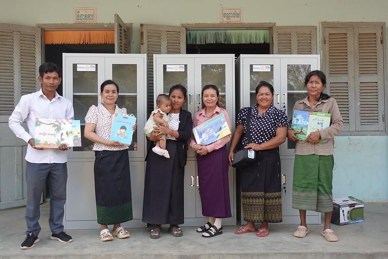 Teachers stand in front of lockable cabinets holding storybooks they received from the project
