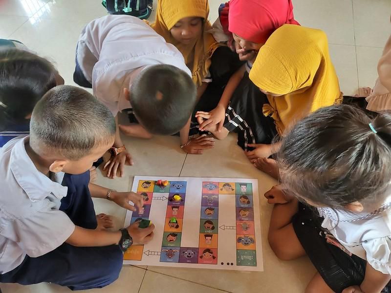Preschool children crowd around a floor board game during a class using R4C materials