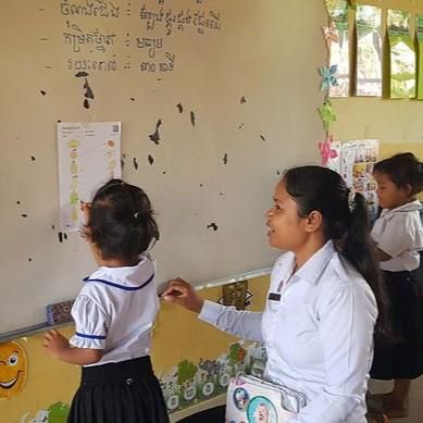 A teacher and a young child place a card on the classroom wall during a lesson